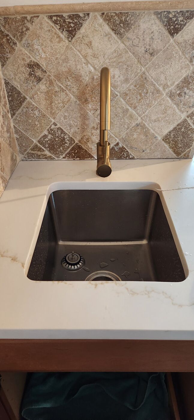 Bar sink with brushed brass faucet and stone tile backsplash